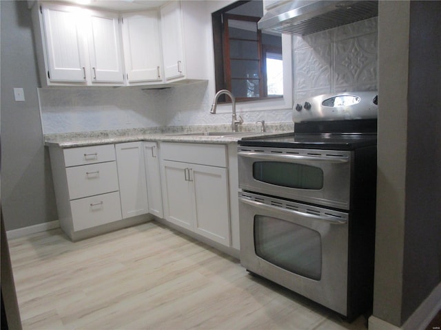 kitchen with under cabinet range hood, double oven range, a sink, tasteful backsplash, and white cabinets