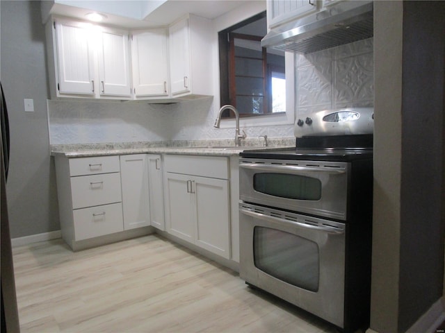 kitchen featuring light wood finished floors, range with two ovens, a sink, under cabinet range hood, and backsplash