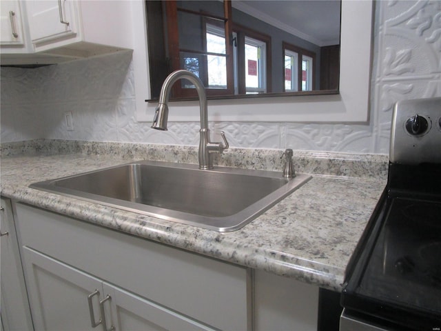 interior details featuring white cabinetry, light countertops, ornamental molding, and a sink