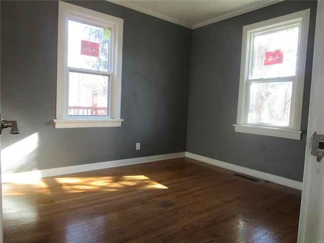 spare room with dark wood finished floors, visible vents, plenty of natural light, and ornamental molding