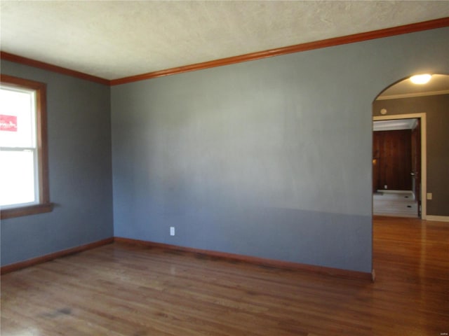 unfurnished room with arched walkways, crown molding, baseboards, and wood finished floors