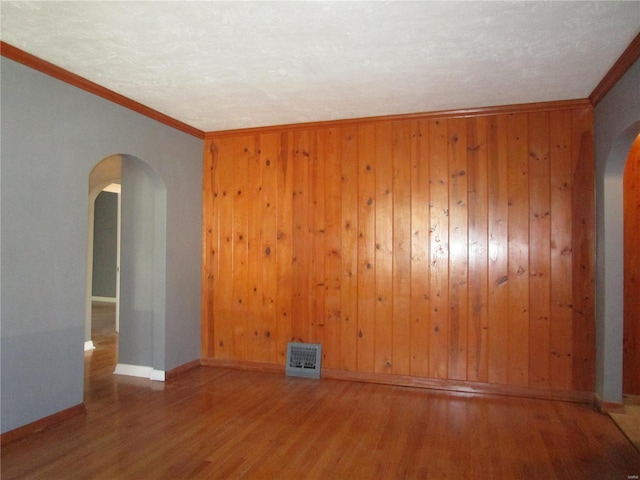 unfurnished room with visible vents, wood finished floors, arched walkways, and ornamental molding