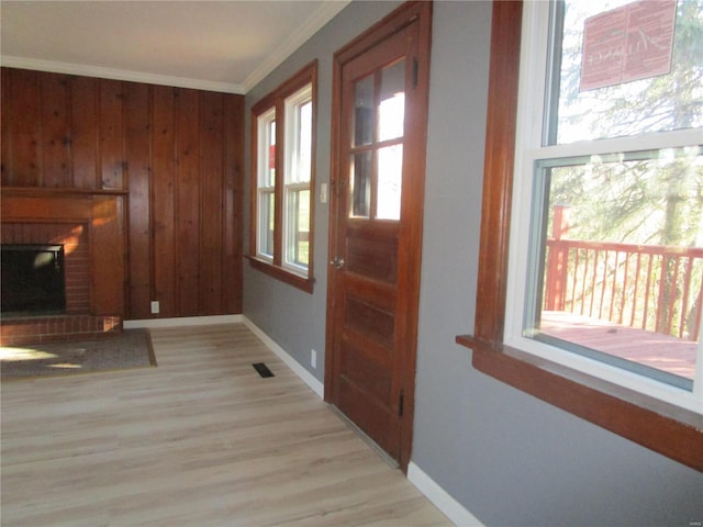 interior space with wooden walls, baseboards, light wood-style flooring, a fireplace, and crown molding