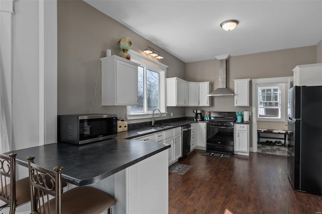 kitchen featuring dark countertops, wall chimney exhaust hood, a peninsula, black appliances, and a sink