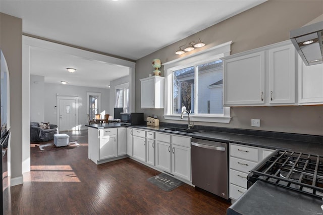 kitchen featuring white cabinets, dark countertops, a peninsula, stainless steel dishwasher, and a sink