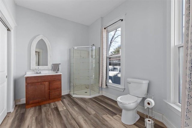 bathroom with toilet, vanity, a shower stall, wood finished floors, and baseboards