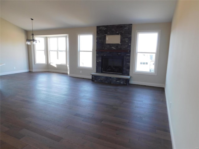 unfurnished living room with baseboards, dark wood-style flooring, a fireplace, and a notable chandelier