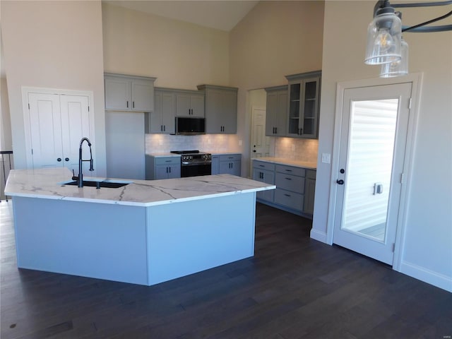 kitchen with a center island with sink, light stone countertops, gray cabinetry, black range with electric cooktop, and a sink