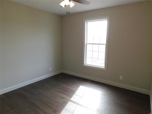 spare room featuring dark wood-style flooring, a ceiling fan, and baseboards