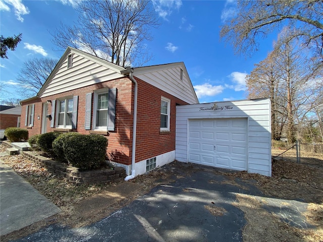 view of property exterior featuring a garage, brick siding, fence, and aphalt driveway