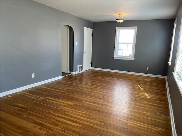 empty room with arched walkways, wood finished floors, visible vents, and baseboards