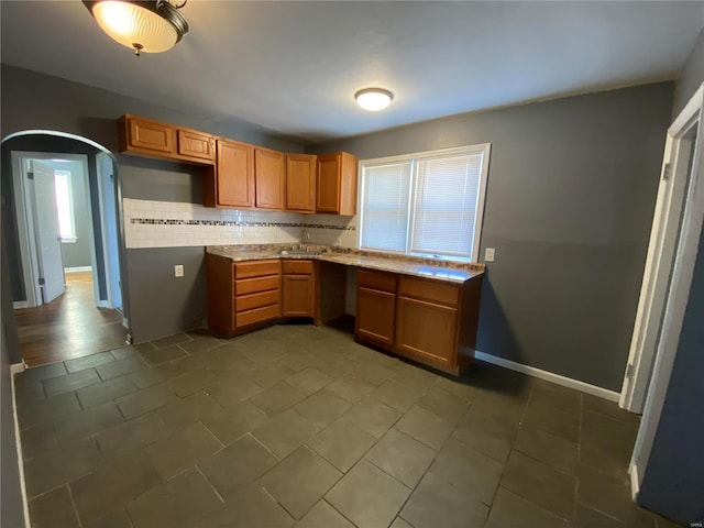 kitchen featuring arched walkways, baseboards, backsplash, and a healthy amount of sunlight