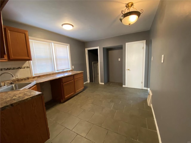 kitchen featuring brown cabinets, baseboards, backsplash, and a sink