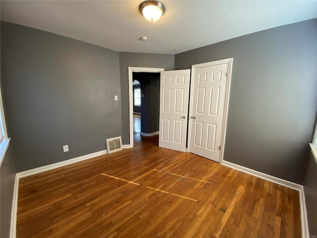 unfurnished bedroom featuring baseboards, a closet, visible vents, and wood finished floors