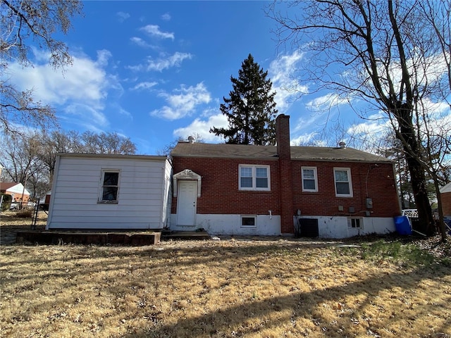 rear view of house with cooling unit, brick siding, a lawn, and a chimney