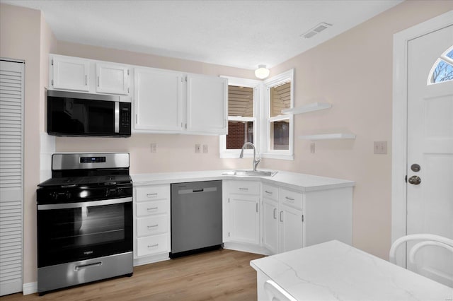 kitchen featuring light wood finished floors, stainless steel appliances, visible vents, white cabinets, and a sink