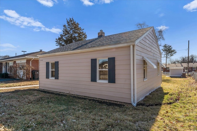 view of side of property with roof with shingles, a lawn, and a chimney