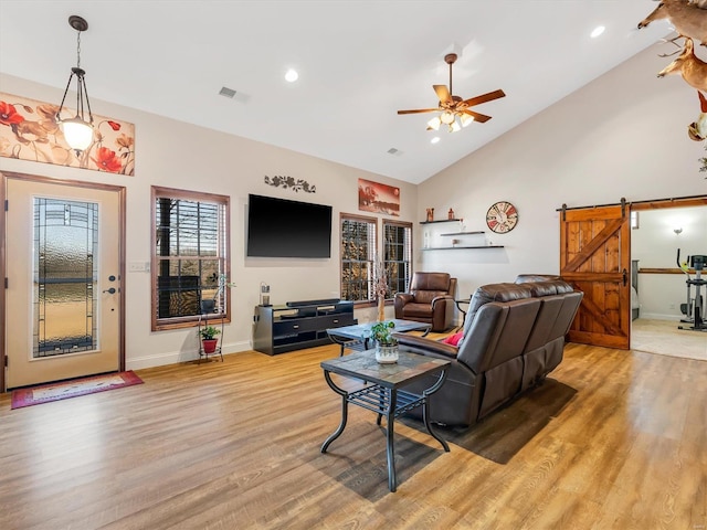 living area with visible vents, a barn door, ceiling fan, high vaulted ceiling, and light wood-type flooring