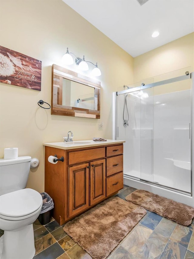 bathroom featuring vanity, stone finish floor, a shower stall, and toilet