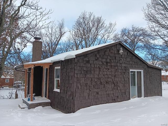 view of snow covered exterior with a chimney and fence