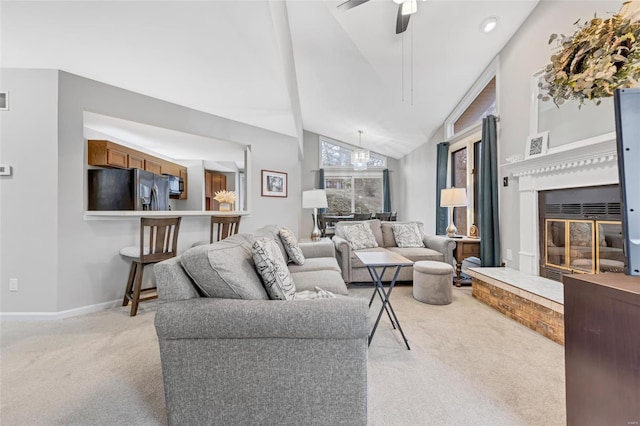 living area with lofted ceiling, ceiling fan, light colored carpet, baseboards, and a glass covered fireplace