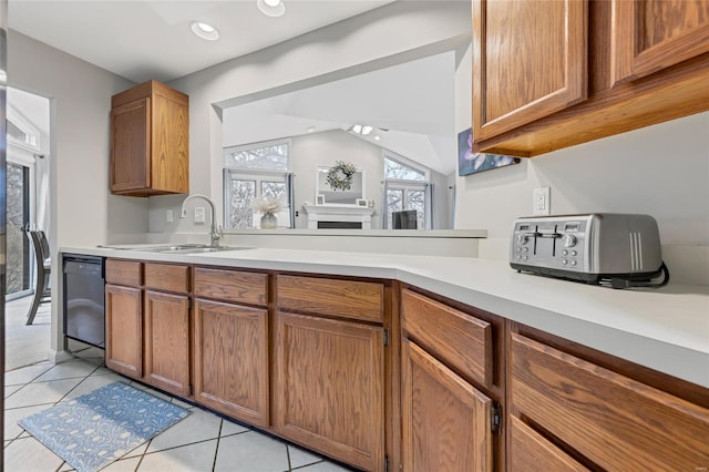 kitchen with light tile patterned floors, dishwasher, brown cabinets, light countertops, and a sink