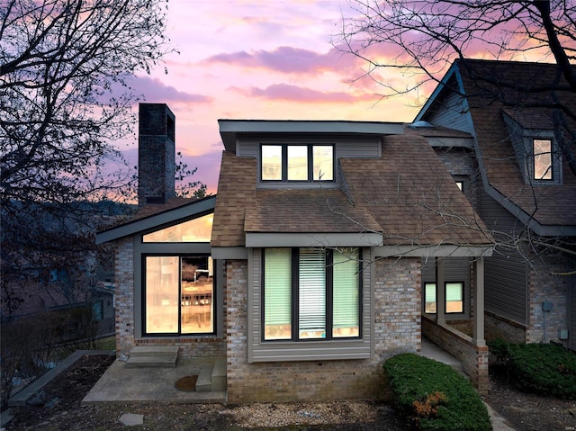 back of property at dusk with a chimney and brick siding