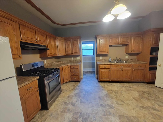 kitchen with stainless steel gas range oven, brown cabinetry, freestanding refrigerator, under cabinet range hood, and a sink