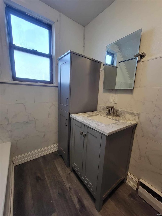 bathroom with a baseboard heating unit, wood finished floors, vanity, and tile walls