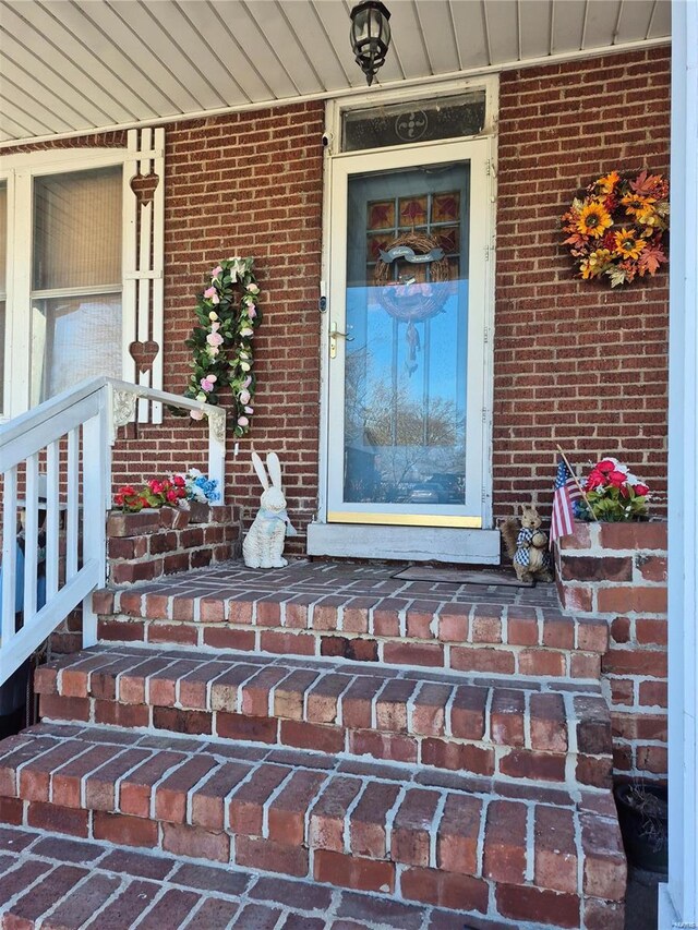 doorway to property featuring a porch and brick siding