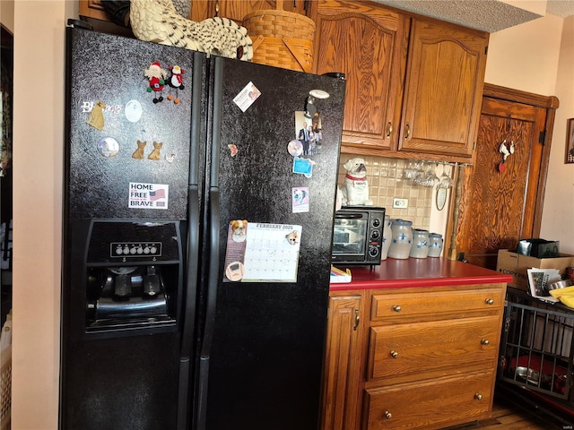 kitchen with a toaster, tasteful backsplash, dark countertops, black refrigerator with ice dispenser, and brown cabinetry