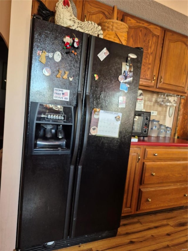 kitchen with arched walkways, brown cabinets, decorative backsplash, black refrigerator with ice dispenser, and dark countertops