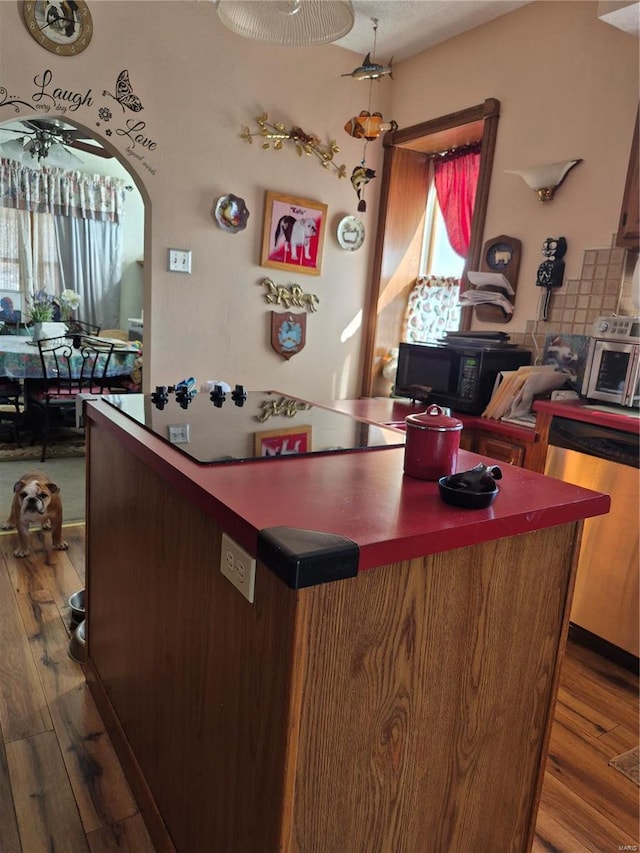 interior space with arched walkways, black microwave, stainless steel dishwasher, and wood finished floors