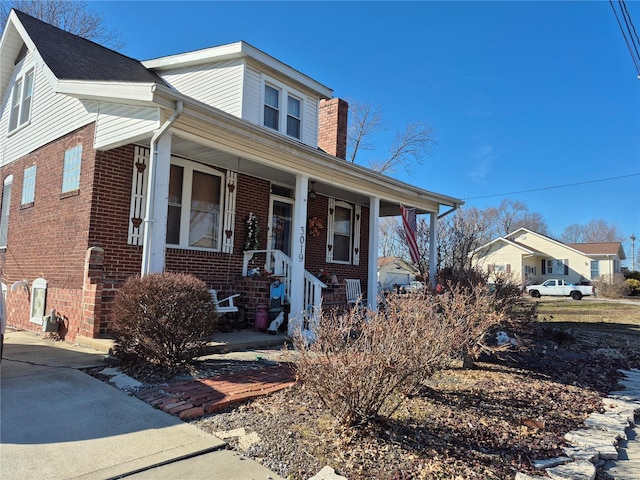 bungalow-style home with covered porch, brick siding, and a chimney