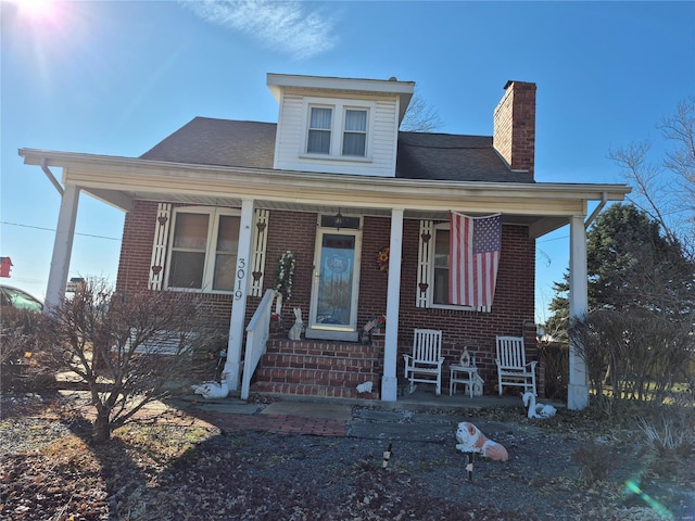 bungalow-style house featuring covered porch, brick siding, and a chimney