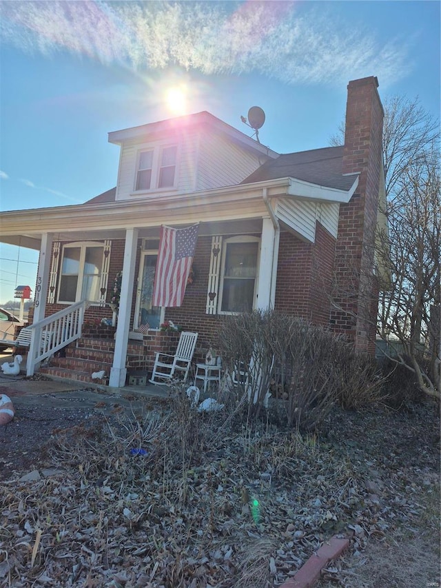 view of front of property featuring a porch, brick siding, and a chimney