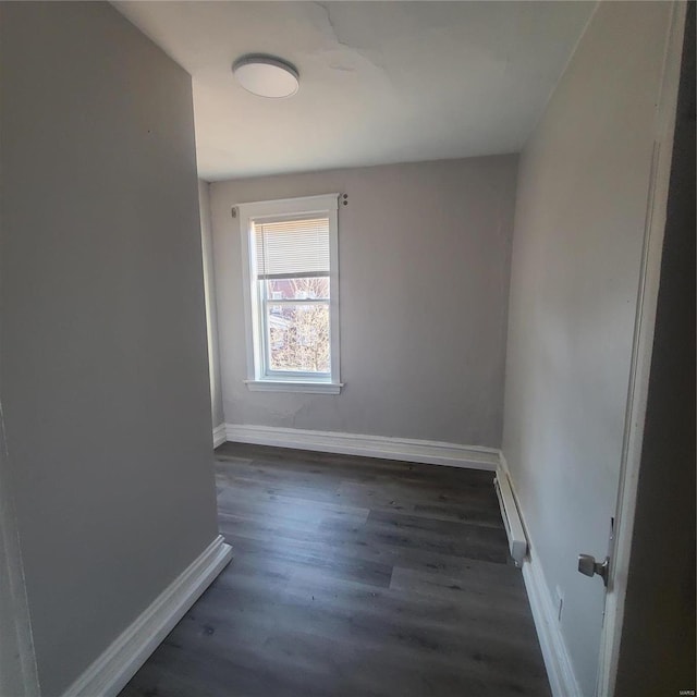 empty room with a baseboard heating unit, dark wood-style flooring, and baseboards