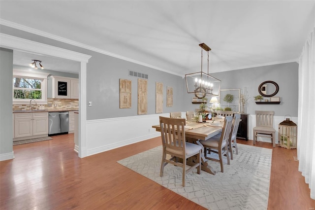 dining area featuring crown molding, a notable chandelier, visible vents, and light wood-style floors