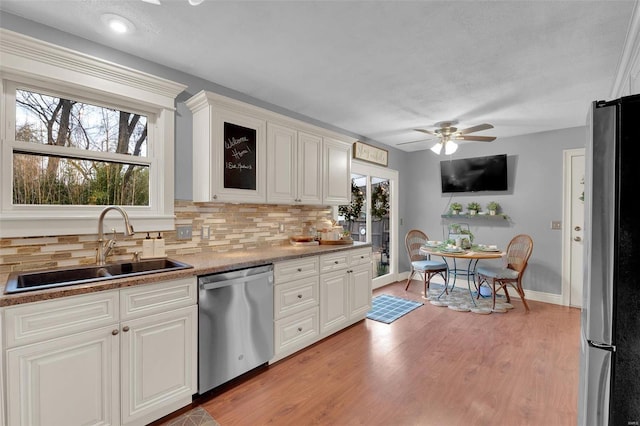 kitchen featuring a sink, light wood-style floors, appliances with stainless steel finishes, decorative backsplash, and glass insert cabinets