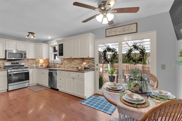 kitchen featuring stainless steel appliances, tasteful backsplash, white cabinets, a sink, and light wood-type flooring