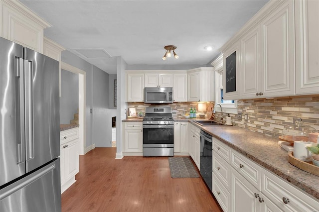 kitchen with light wood finished floors, white cabinets, decorative backsplash, stainless steel appliances, and a sink