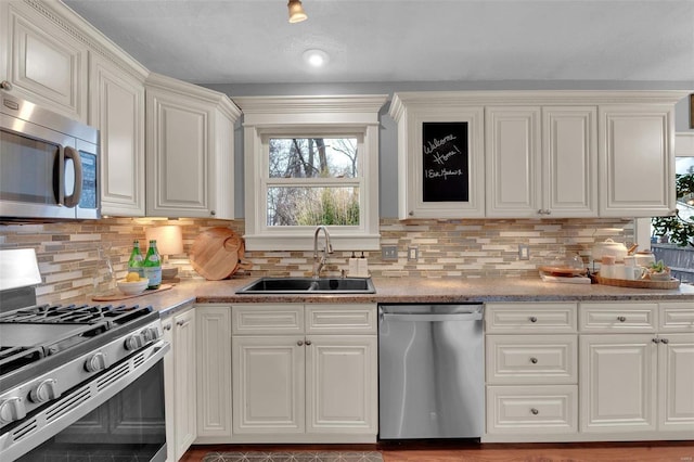 kitchen with appliances with stainless steel finishes, white cabinets, a sink, and backsplash