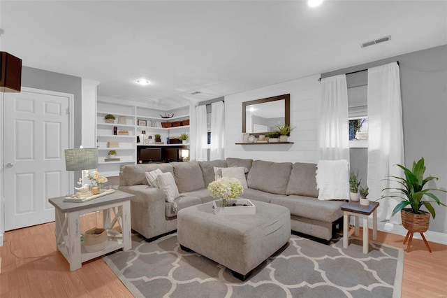 living area featuring built in shelves, light wood-type flooring, and visible vents