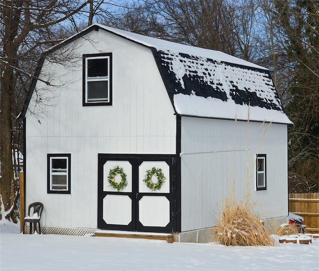 view of snowy exterior featuring an outbuilding, fence, and a gambrel roof