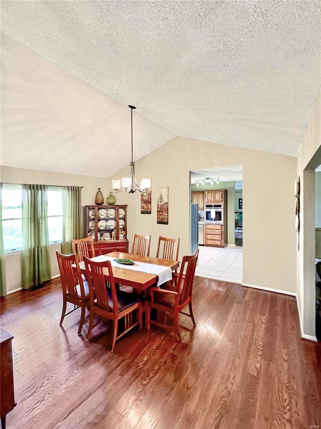 dining area featuring lofted ceiling, an inviting chandelier, light wood-style flooring, and a textured ceiling