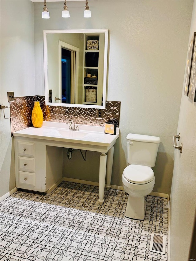 half bath featuring toilet, baseboards, visible vents, and decorative backsplash