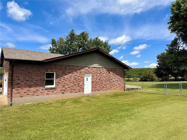 view of property exterior featuring a shingled roof, a gate, fence, a yard, and brick siding