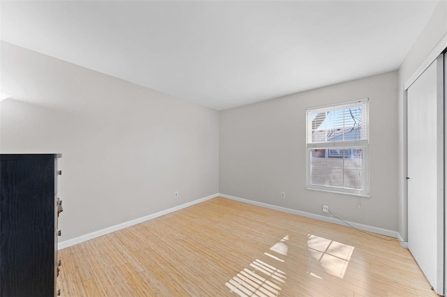 unfurnished bedroom featuring light wood-style flooring, baseboards, and a closet