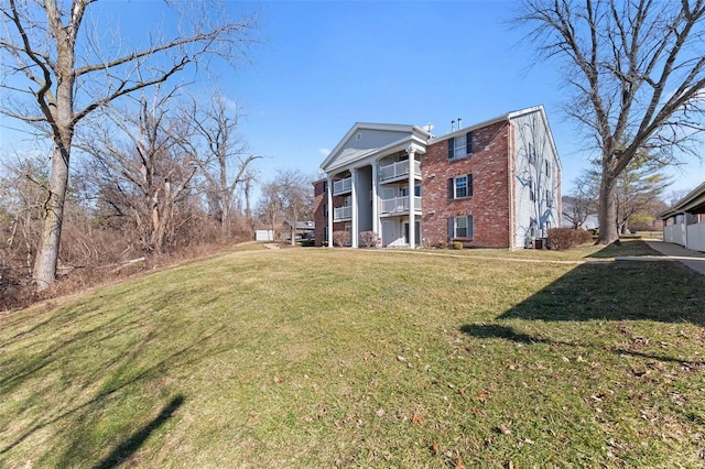 rear view of property with a balcony, a yard, and brick siding