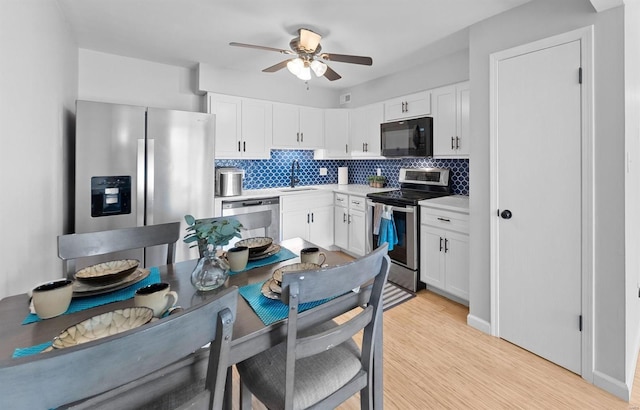 kitchen with light wood-style flooring, a sink, appliances with stainless steel finishes, white cabinetry, and tasteful backsplash